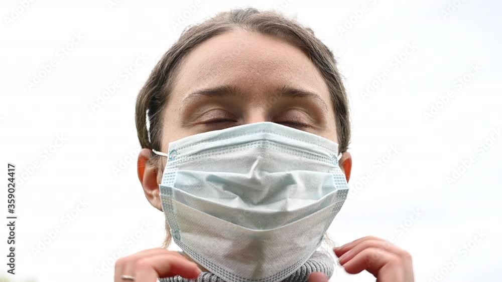 Woman wearing an antiviral blue medical mask outside in a green park