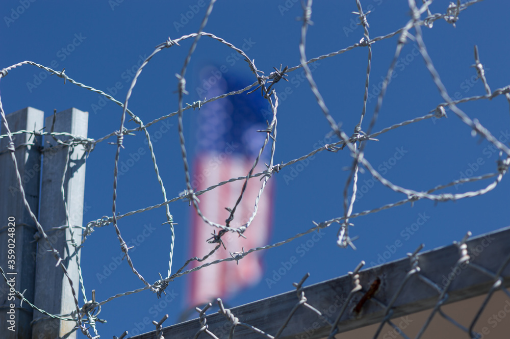 Looped barbed wire fence in front of American flag Looped barbed wire fence in front of American flag