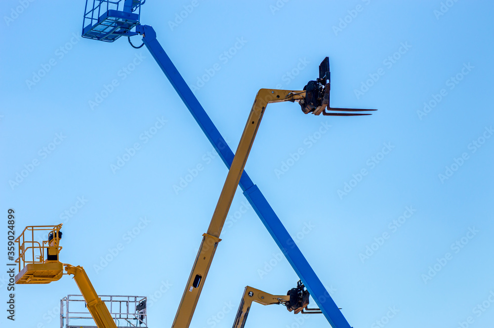 Aerial work platforms and cranes isolated against blue sky