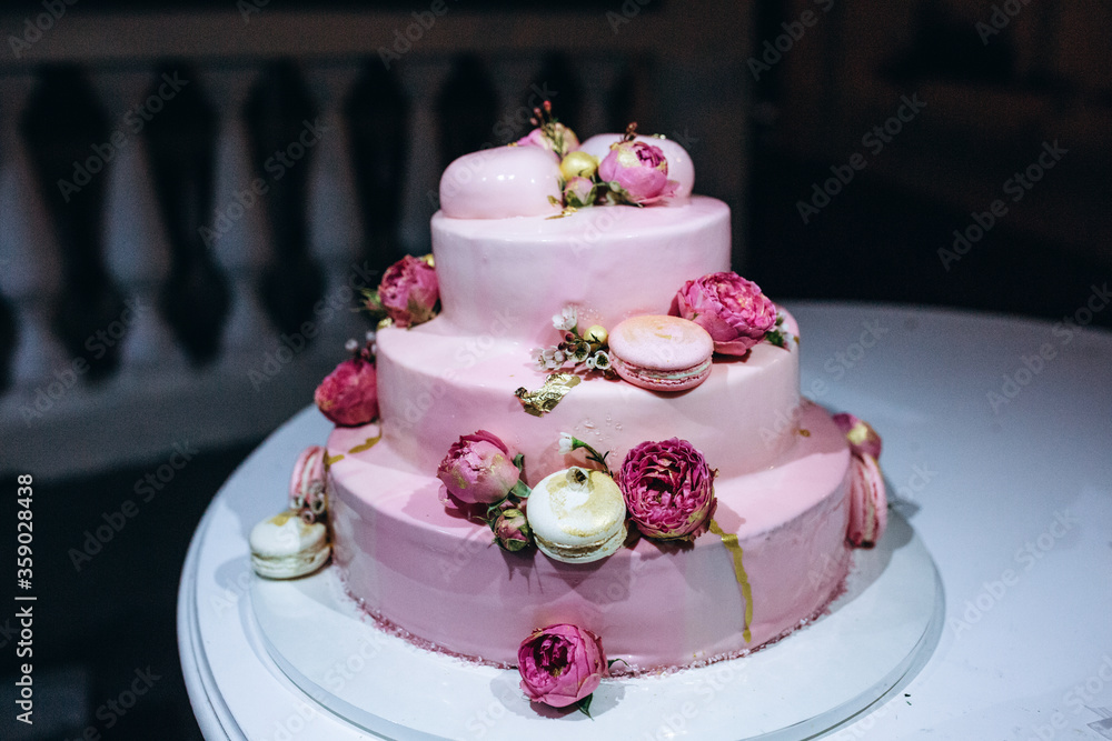 Layered wedding cake on the table. Delicate pink cream, decoration of flowers and cookies. Layered wedding cake on the table. Delicate pink cream, decoration of flowers and cookies.