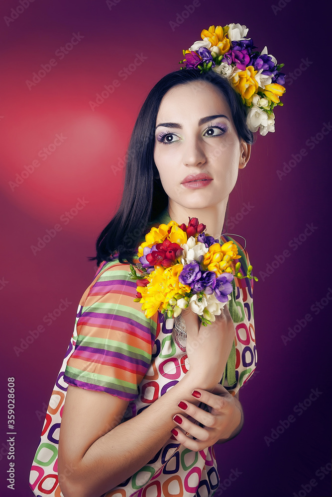Portrait of a cute girl with bright makeup and with the blooming freesias on his head and hands on a red background in the Studio.
