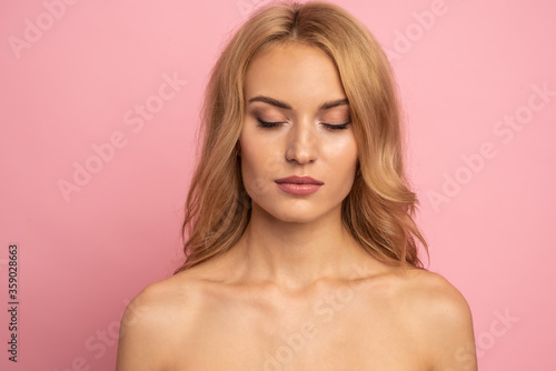 Beautiful sensual topless woman with long blonde hair posing isolated over pink background. Beauty concept
