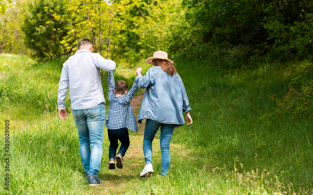 Fototapeta premium Back view of young parents on walk with their child at countryside, copy space