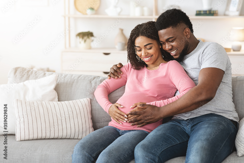 Lovely smiling expecting parents sitting on sofa at home