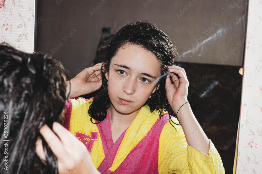 Φωτογραφία A teenage girl with wet washed hair looks at her reflection in the mirror