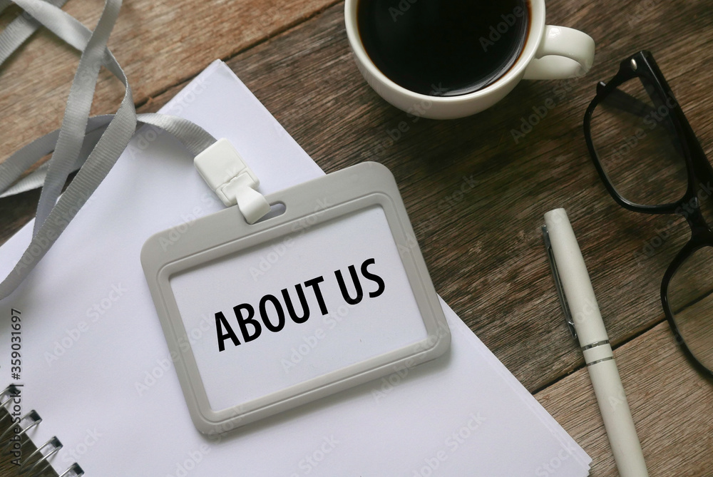 Top view of pen,a cup of coffee,notebook and lanyard with card holder written with About Us on wooden background. Top view of pen,a cup of coffee,notebook and lanyard with card holder written with About Us on wooden background.