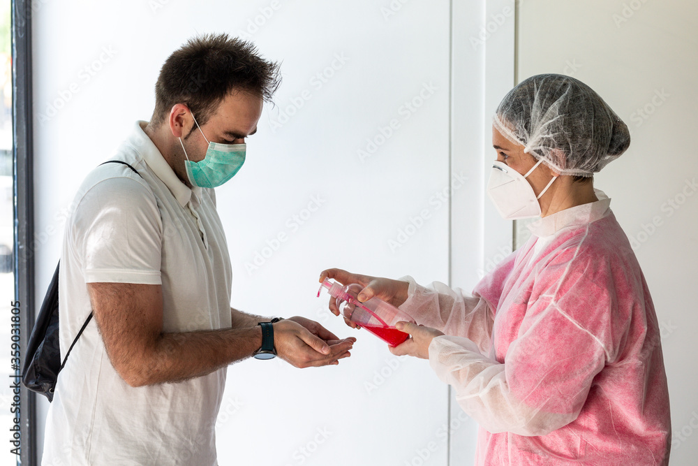 Obraz premium a health worker sprays a patient's hands with hydroalcoholic gel to prevent a coronavirus pandemic. they wear masks, clothing and a protective cap