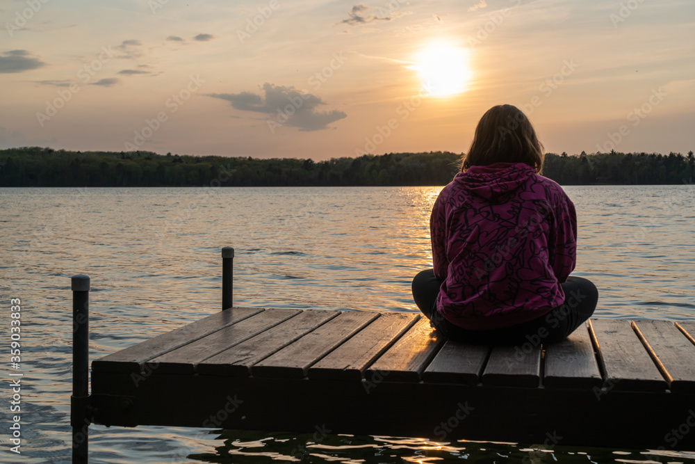 Girl sitting alone on dock facing sunset Stock Photo | Adobe Stock