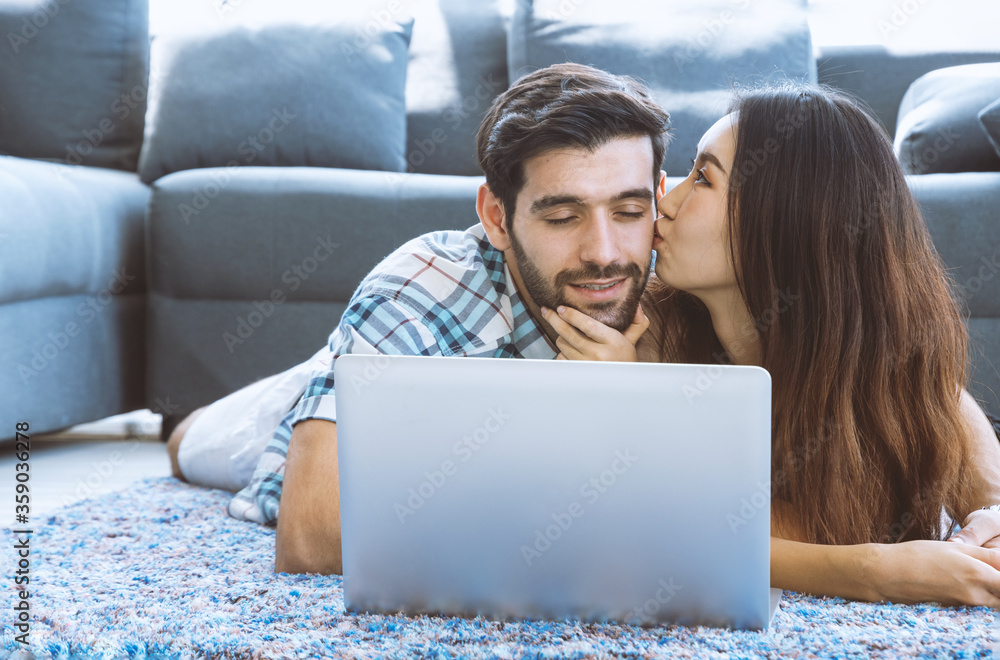 Couple in love lying on the floor using notebook at home. Woman kiss her boyfriend.