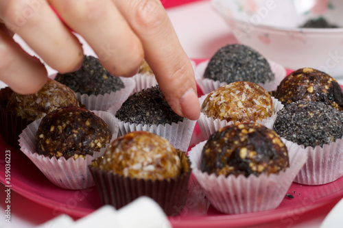 Woman puts dried fruit candies on a plate. Balls of prunes, dates and coconut. With a sprinkle of black sesame powder.