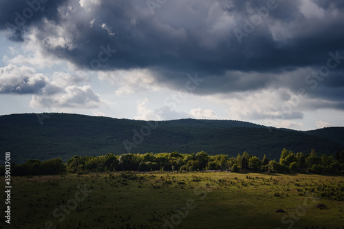 Dramatic sky with dark rain clouds and sunshine illuminating green slopes