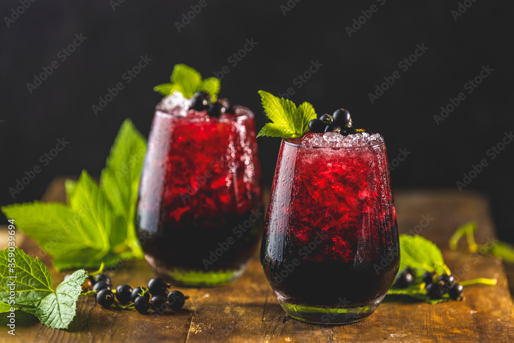 Φωτογραφία Two glass of cold ice black currant juice or cocktail with ripe berries and green leaves on dark wooden table