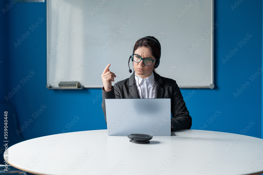 An angry woman in a headset is having an online conversation on a laptop in a conference room. Female boss scolding subordinates for a video call. Unsuccessful remote business negotiations. An angry woman in a headset is having an online conversation on a laptop in a conference room. Female boss scolding subordinates for a video call. Unsuccessful remote business negotiations.