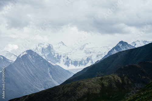 Wonderful view to huge glaciers on great snowy mountain range behind big rocks under gloomy cloudy sky. Pointy tops of giant rocky mountains. Awesome beauty of highlands. Atmospheric alpine landscape.