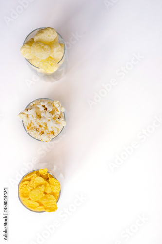 Three glass glasses filled with popcorn, corn flakes and corn sticks. A light, delicious snack. Corn products.