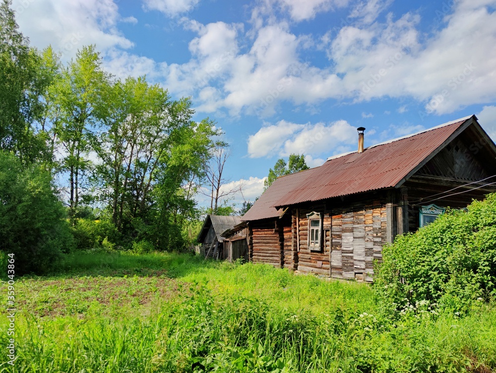green courtyard near an old wooden house and trees against a blue sky with clouds on a sunny day green courtyard near an old wooden house and trees against a blue sky with clouds on a sunny day