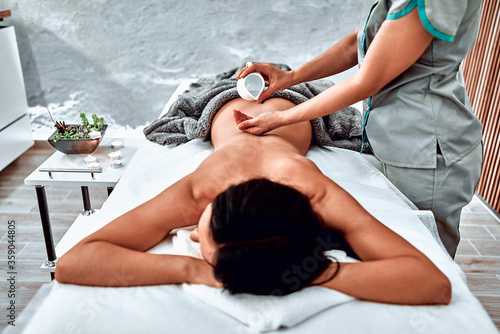 Professional masseur applying massage oil on female back in the beauty salon