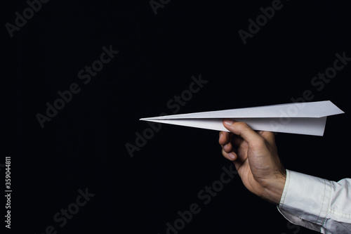 A male hand holds a paper airplane on a black background.