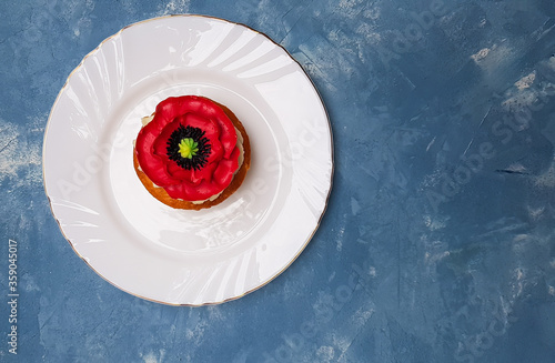 Beautiful decorated cupcake with red poppy flower on white plate on blue background
