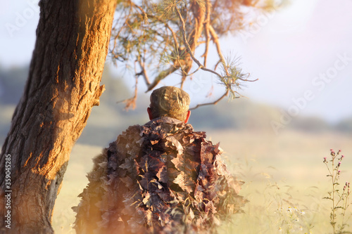 Hunter observes animals under pine in a camouflage suit.