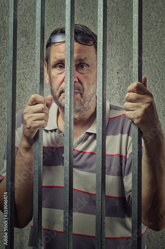 Elderly Prisoner with Seasoned Expression Stands Behind Bars, Calmly Reflecting on His Experience and Confidence in a Difficult Situation.