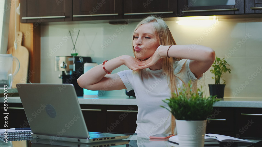 Cheerful woman singing and gesturing while looking on the computer screen. She spending her free time in the kitchen. Cheerful woman singing and gesturing while looking on the computer screen. She spending her free time in the kitchen.
