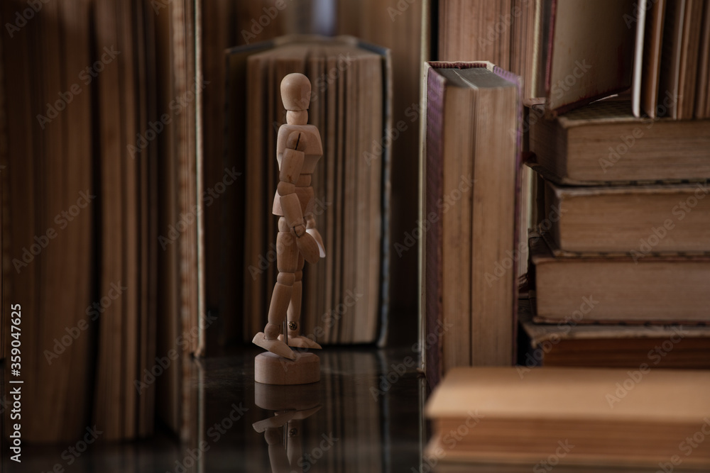 A drawing mannequin in between a bunch of old upright books A drawing mannequin in between a bunch of old upright books