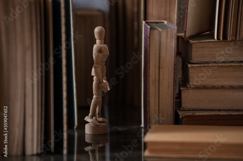 A drawing mannequin in between a bunch of old upright books
