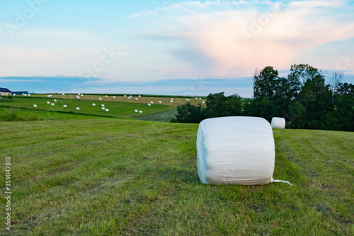 Country landscape. Hills and meadows. Beautiful sky. Summer. Big white bale of grass silage left on the meadow. Mowed meadow. Haying time. Countryside holidays.