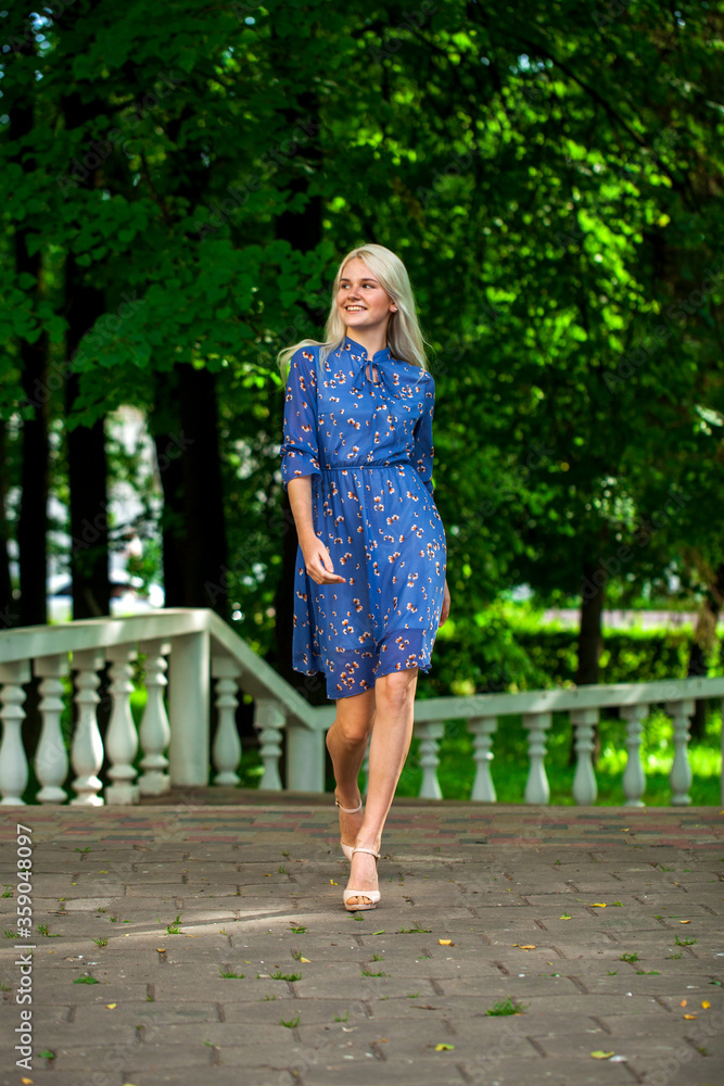 Portrait of a young blonde woman in blue dress walking in summer parkpark Portrait of a young blonde woman in blue dress walking in summer parkpark