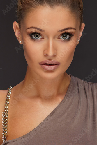 Obraz na płótnie Portrait of beautiful sexy blonde girl with tied up hair and tanned body wearing brown shirt, sensual posing on black wall. w salonie