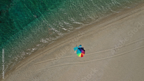 Aerial top down photo of beautiful turquoise Mediterranean secluded sandy bay forming a small peninsula with only one colourful sun umbrella enjoying summer