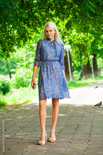 Portrait of a young blonde woman in blue dress walking in summer parkpark © Andrey_Arkusha