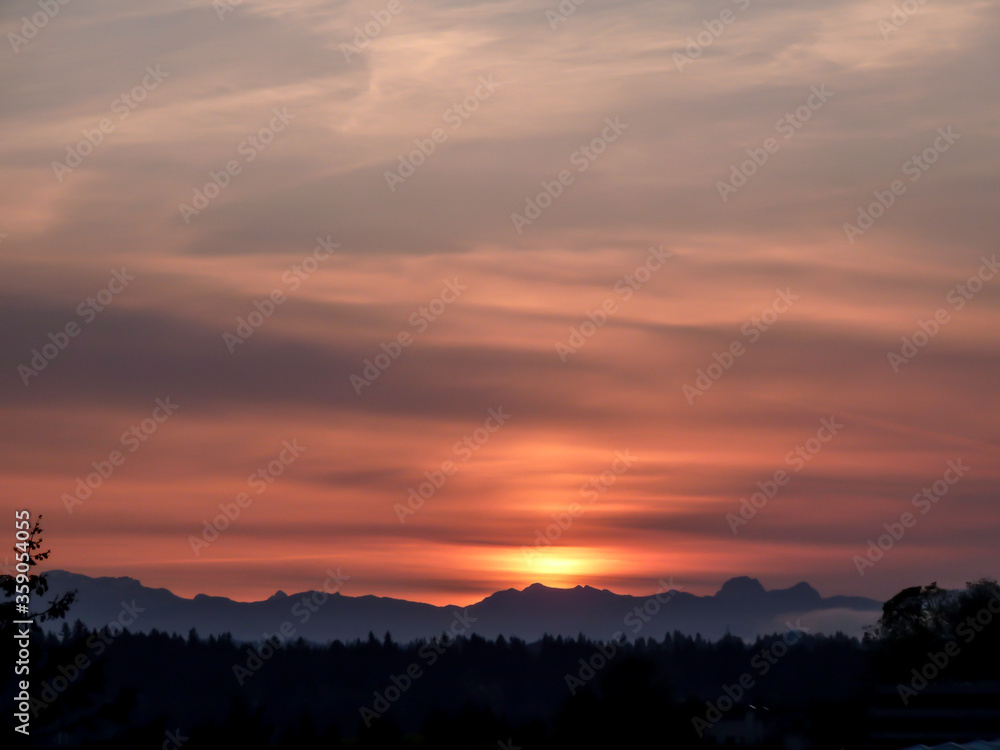 Sky with streaky clouds in a grayish and orange-red sky during sunrise over Cascade Range in Washington State.