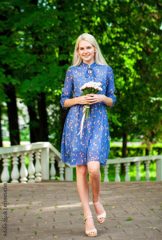 Portrait of a young blonde woman in blue dress walking in summer parkpark Portrait of a young blonde woman in blue dress walking in summer parkpark