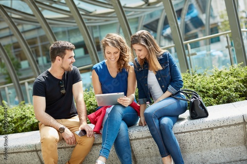 Outdoor photo of happy friends using tablet on the street. 