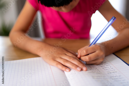 girl working studiously at home, writing with her left hand on a homework notebook