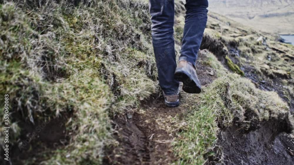 Man's Legs Walking in Grassy Cliff with Blurred View of Faroe Island Seas Man's Legs Walking in Grassy Cliff with Blurred View of Faroe Island Seas