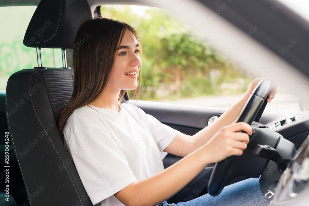 Naklejka premium Driving around city. Young attractive woman smiling and looking straight while driving a car