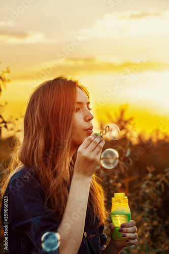 Portrait of a beautiful girl having fun outdoors blowing soap bubbles. Pretty young woman