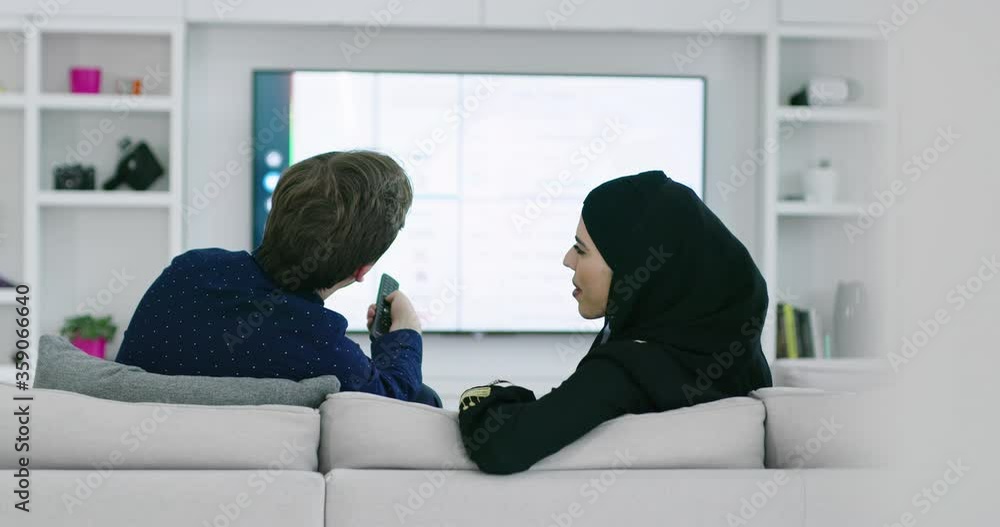 Young muslim couple watching TV on sofa before iftar Young muslim couple watching TV on sofa before iftar