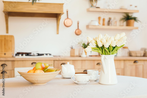 bright wooden kitchen in the style of Provence and Scandinavia  on the table dishes  a set of fruit and a bouquet of flowers in a vase. tulips and apples. The concept of a women s holiday