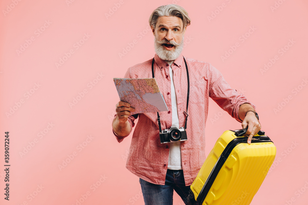 Bearded stylish man holds a yellow suitcase and chooses a country to travel on the map. Bearded stylish man holds a yellow suitcase and chooses a country to travel on the map.