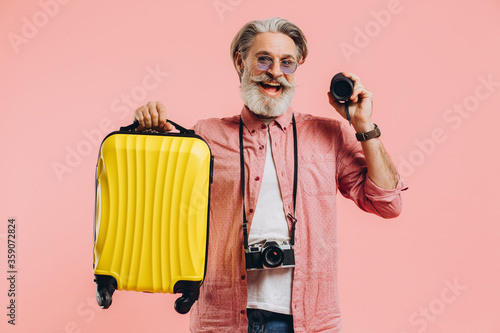 Happy bearded stylish man in sunglasses with camera holding a suitcase and a portable speaker