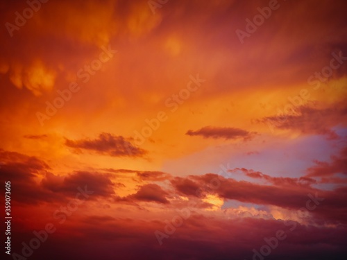 Rain clouds are colored orange by the light of the setting sun over the horizon