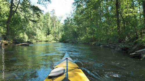 Yellow color nose of kayak moving along in forest calm river on a nice sunny day, outdoor activities