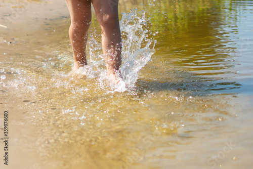 A child runs along the river bank splashing water with his feet