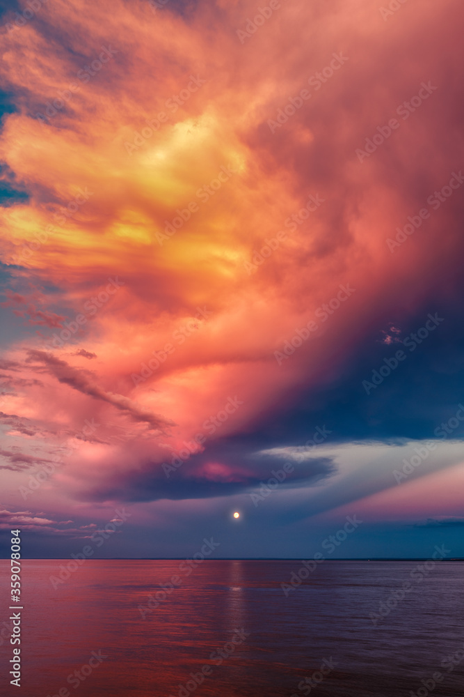 Moon over sea horizon with golden sunset clouds