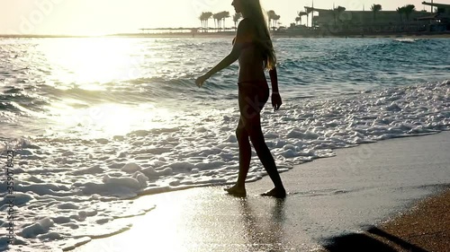 Slow motion of walking girl on sand beaches in sea. Young woman goes into wave water and looks around laughing at end with palm tree background.