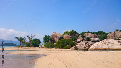 Foto Rocks and palm trees of a sandy sea beach with mountains in the background